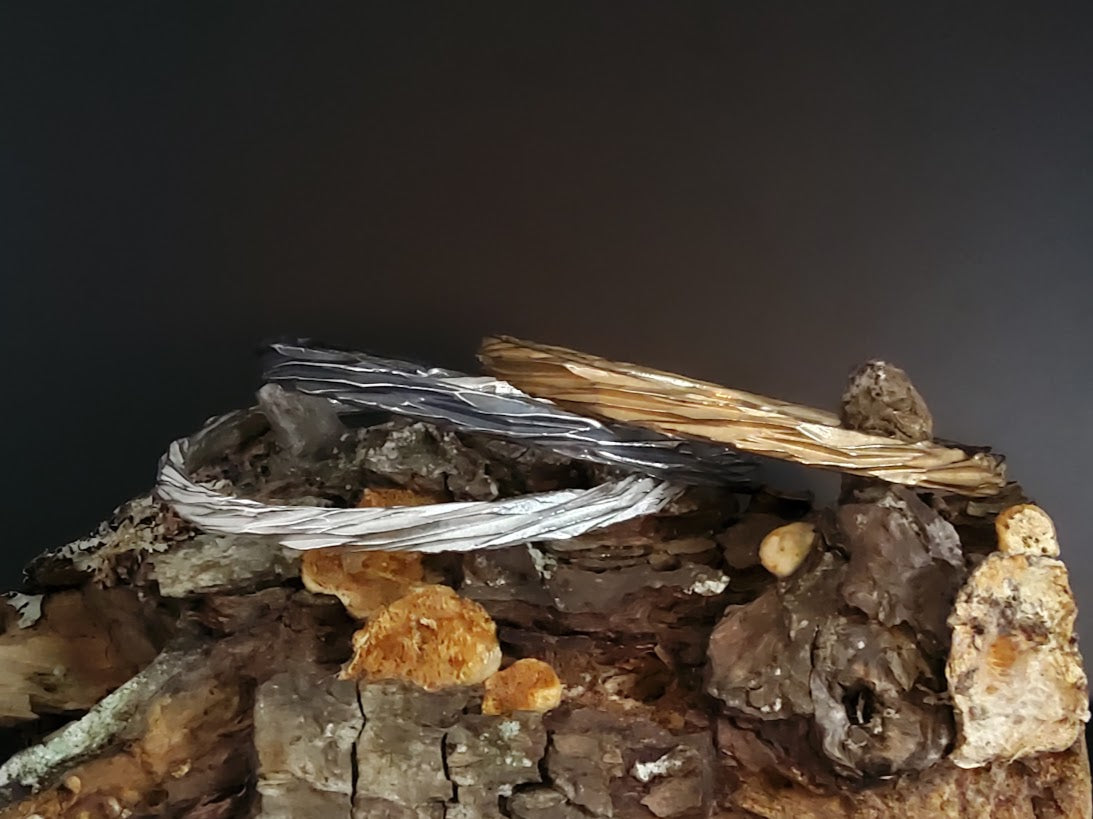 Sterling silver, oxidised and bronze tree bark bangles sitting on an old log by Kara Jewelery