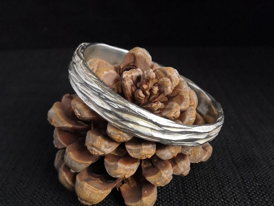 Beech wood silver chunky bangle with a tree bark texture, resting on a pine cone