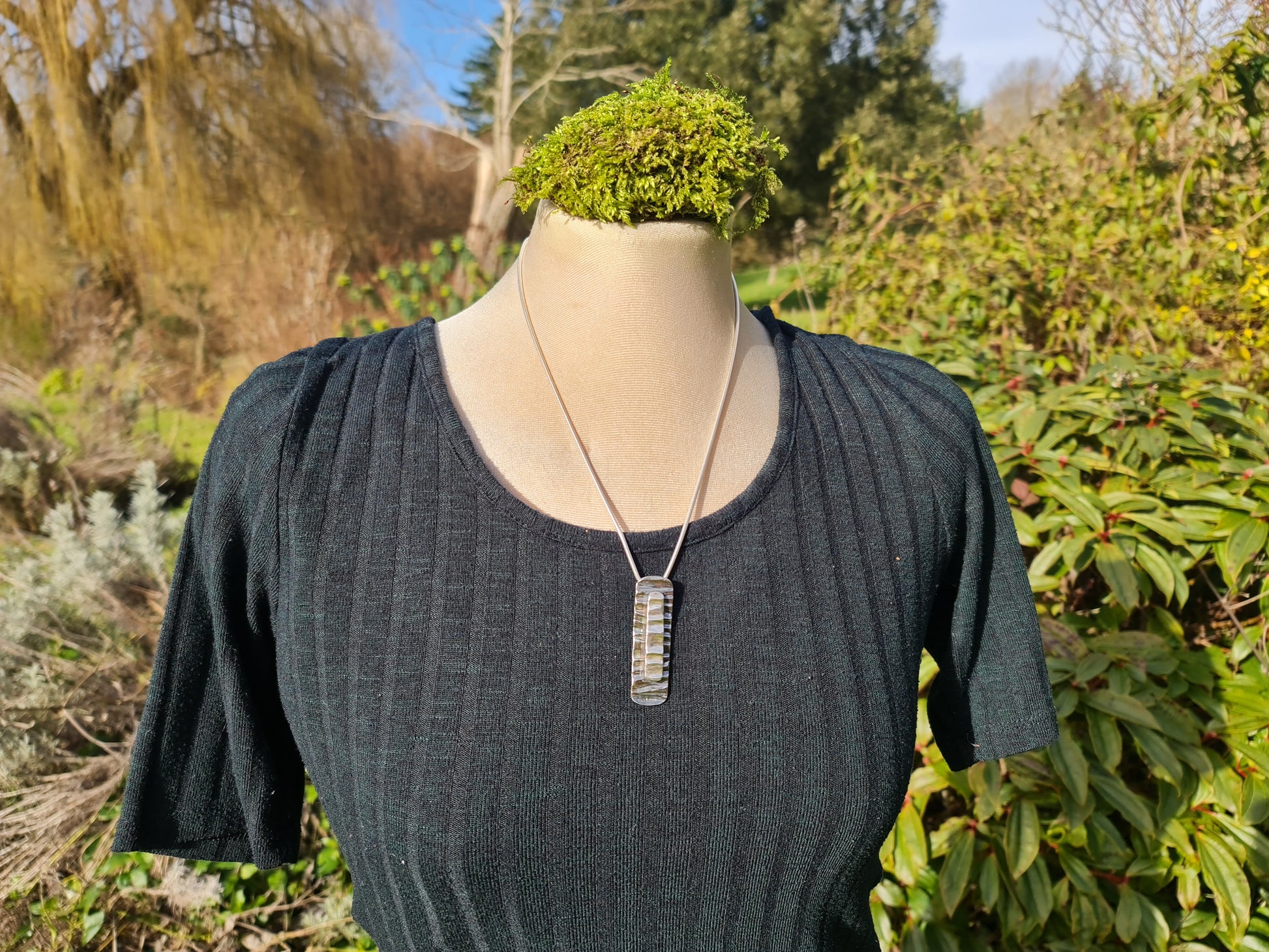 Sterling silver tree bark textured rectangular pendant on a long chain on a black round necked t shirt.