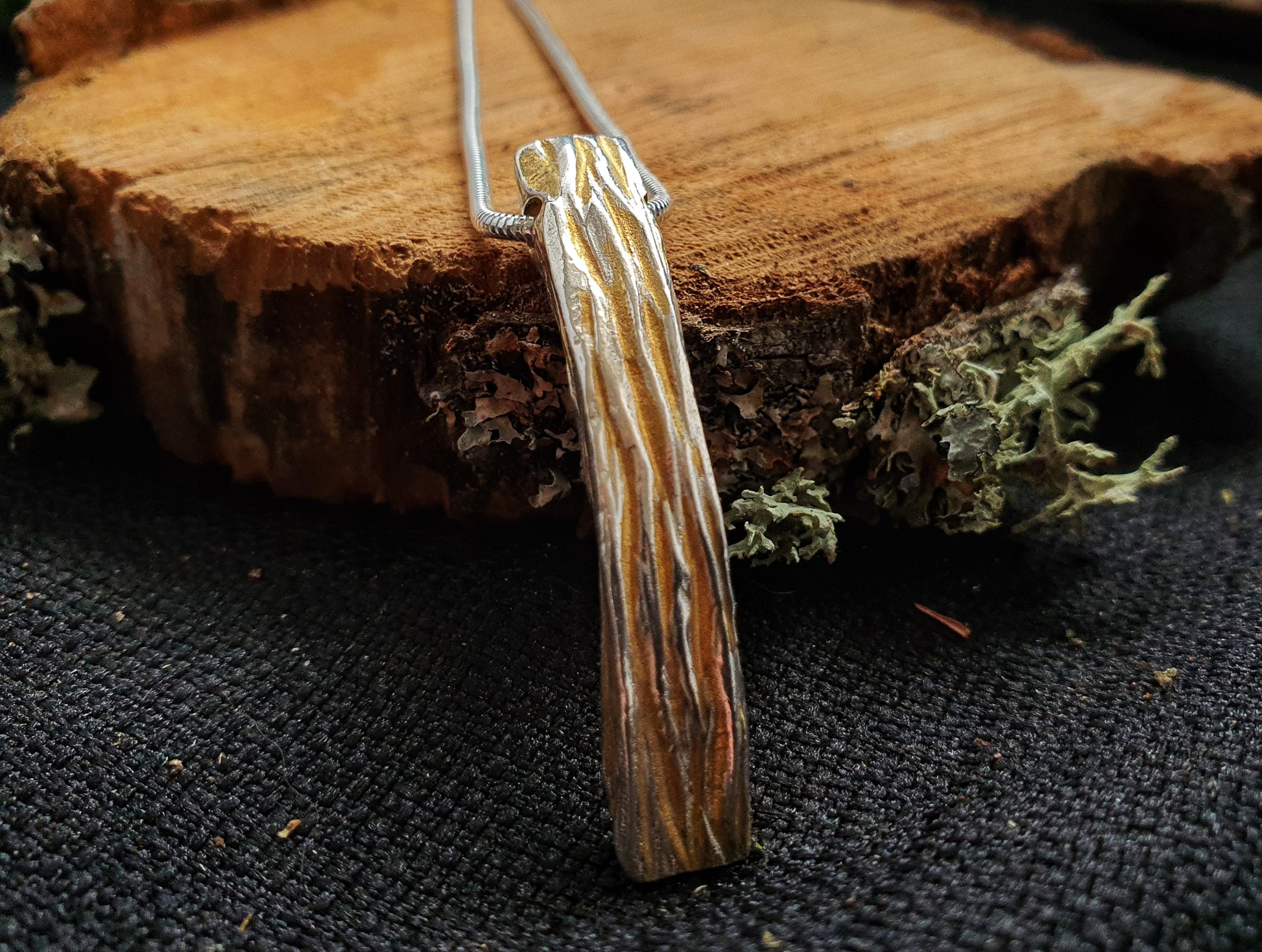 Sterling Silver and Gold Plate two tone tree bark textured pendant sitting on a log slice by Kara Jewellery by Charlotte